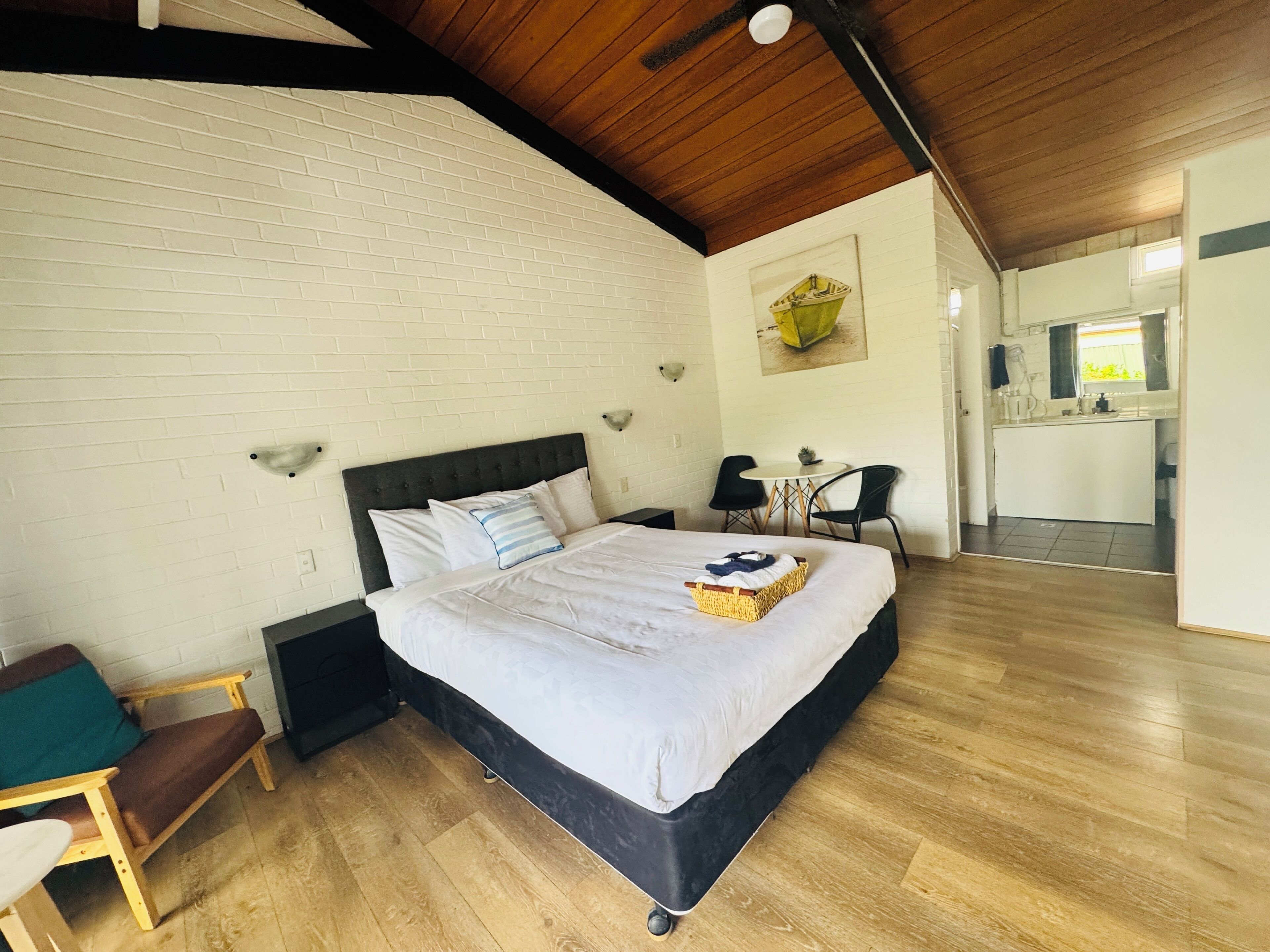 Une chambre avec un lit, une petite table, deux chaises, un coin cuisine et un plafond en bois.