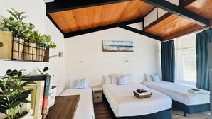 A cozy bedroom with a wooden ceiling, a white brick wall, and a large window with curtains. There are two beds with white bedding and a small table with a basket. - Jetty Motel The Entrance (Long Jetty)