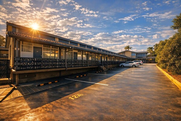 A motel with a covered walkway, a parking lot, and a car parked in the distance.