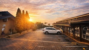 A parking lot with a white SUV, brick buildings, and a sunset. - Jetty Motel The Entrance (Long Jetty)