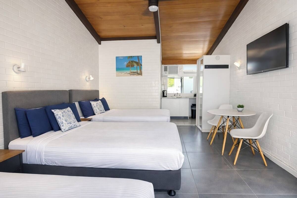 A hotel room with two beds, a small kitchenette, a dining area with a table and chairs, and a TV mounted on the wall.