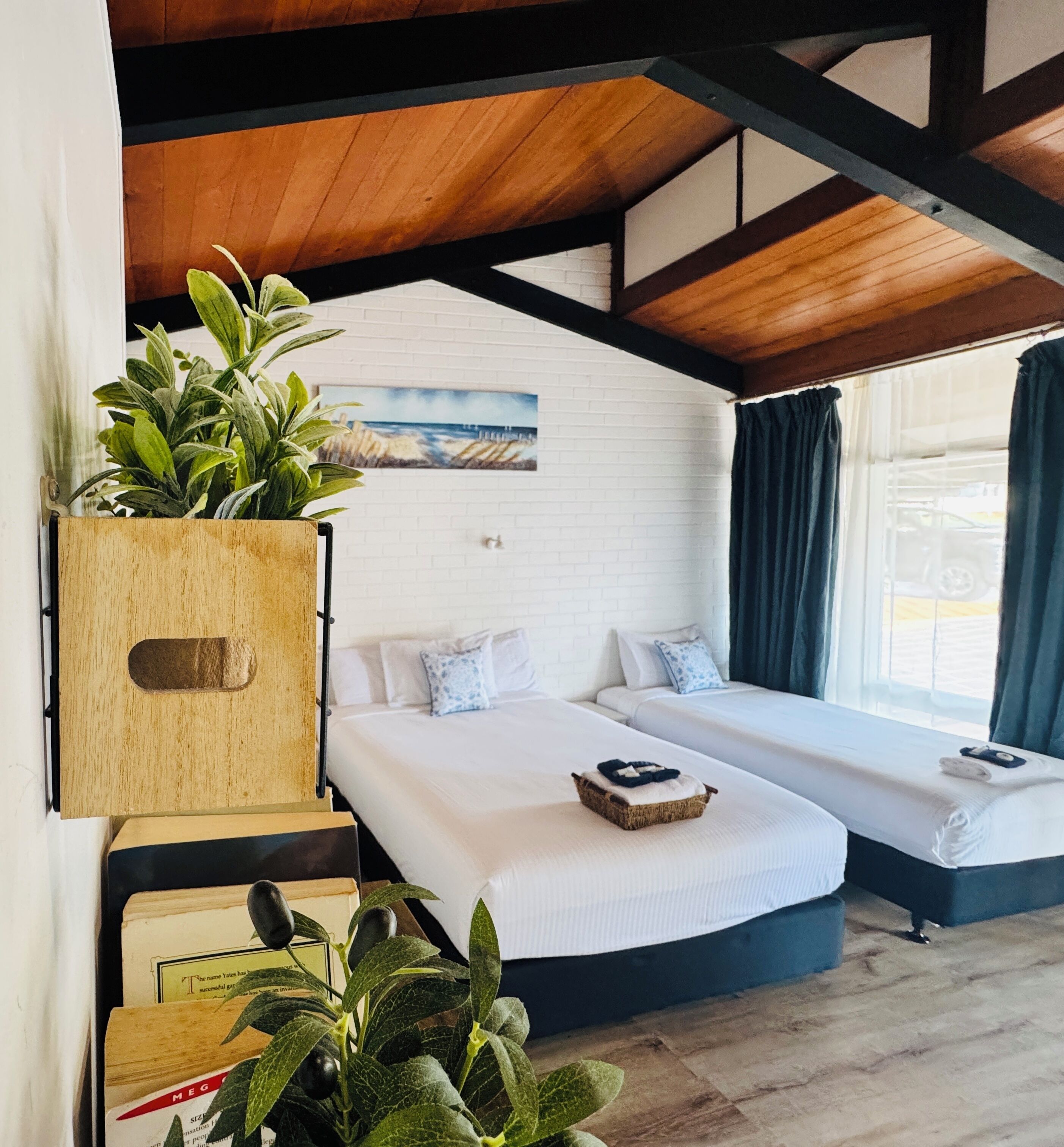 Une pièce avec deux lits, une armoire en bois ornée de plantes, un mur en briques blanches et un tableau.