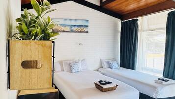 Una habitación con dos camas, un aparador de madera con plantas, un pared de ladrillo blanco y un cuadro.