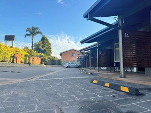 A parking area with a paved surface, a car, and a building with numbered rooms.
