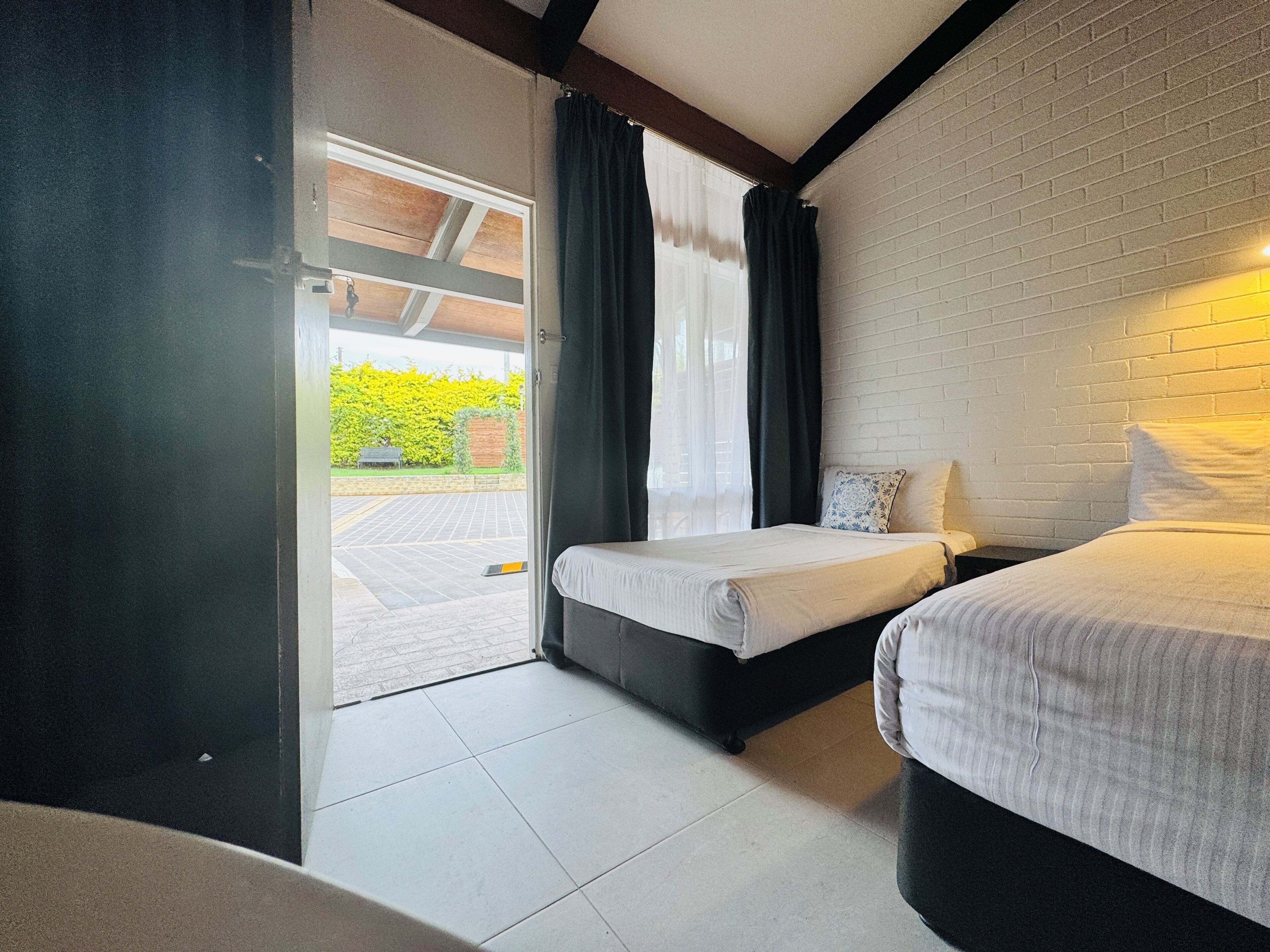 A room with two beds, a white brick wall, and a view of a parking area.