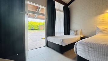 A room with two beds, a white brick wall, and a view of a parking area.