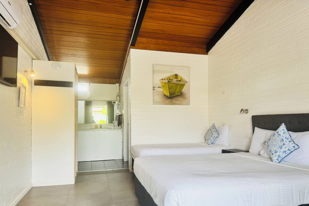 A bedroom with a bed, a nightstand, a wall-mounted lamp, and a picture of a boat.