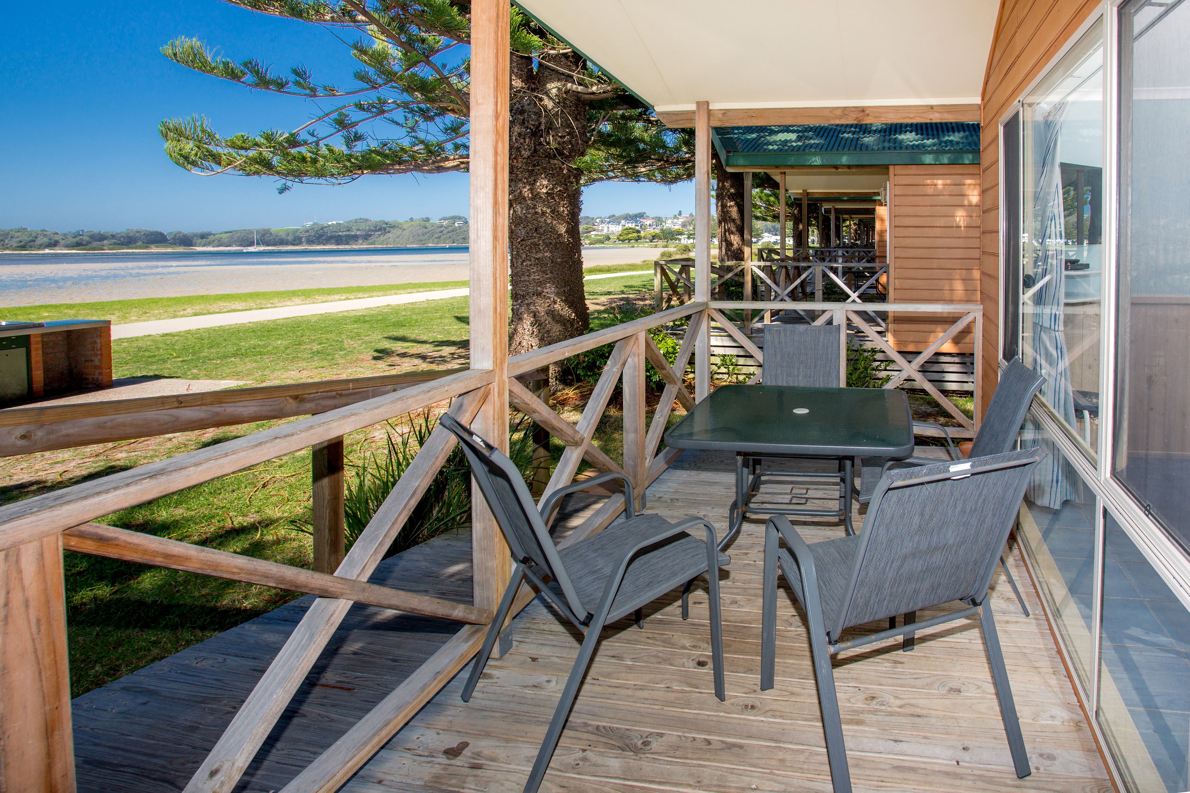 A wooden deck with a table and chairs, overlooking a body of water and a distant shoreline.