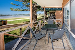 A wooden deck with a table and chairs, overlooking a body of water and a distant shoreline.