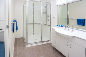 A modern bathroom with a glass shower enclosure, a white sink, and a large mirror.