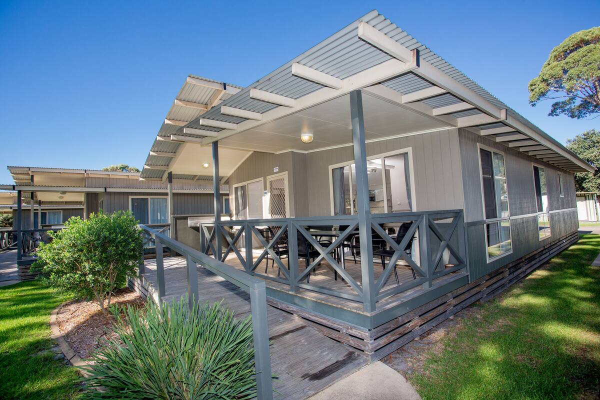 A modern building with a covered patio area, a small garden, and a clear sky.