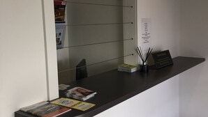 Un comptoir d’accueil avec un miroir, des magazines, une petite plante et un panneau.