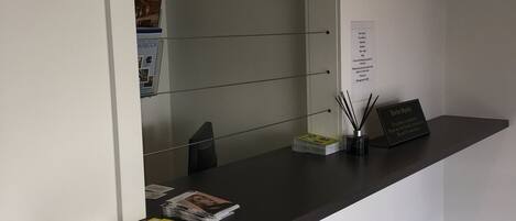 A reception desk with a mirror, magazines, a small plant, and a sign.