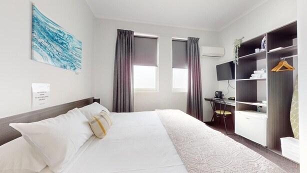 Une chambre d’hôtel avec un lit, un bureau, une armoire et une grande fenêtre avec des rideaux.