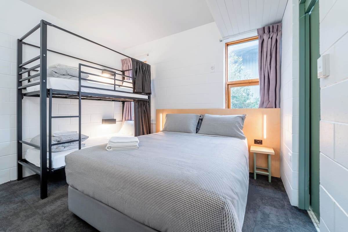 A bunk bed with a lower bunk, a bedside table with a lamp, and a window with curtains.