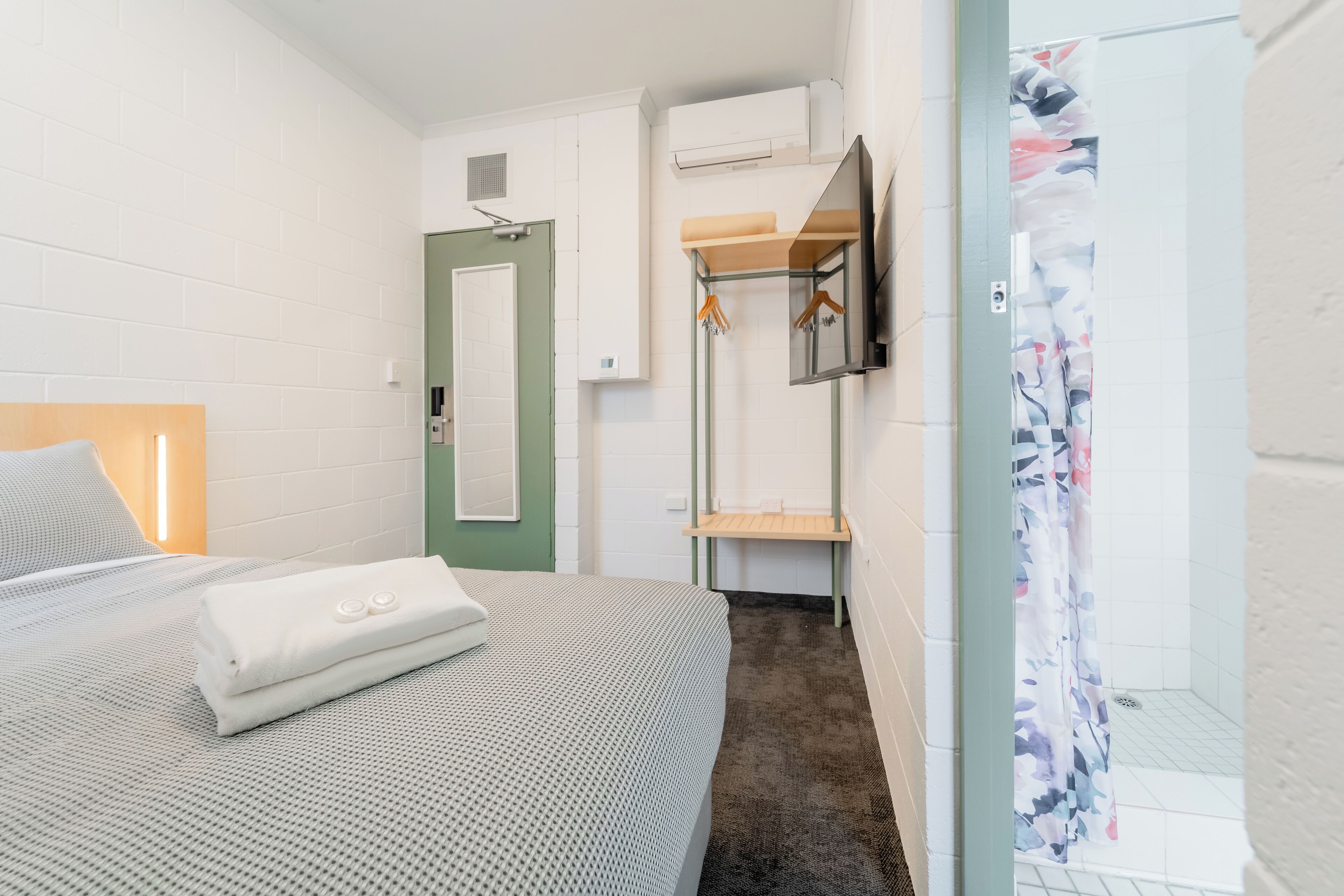 Habitación de hotel con cama, zona de ducha y espejo.