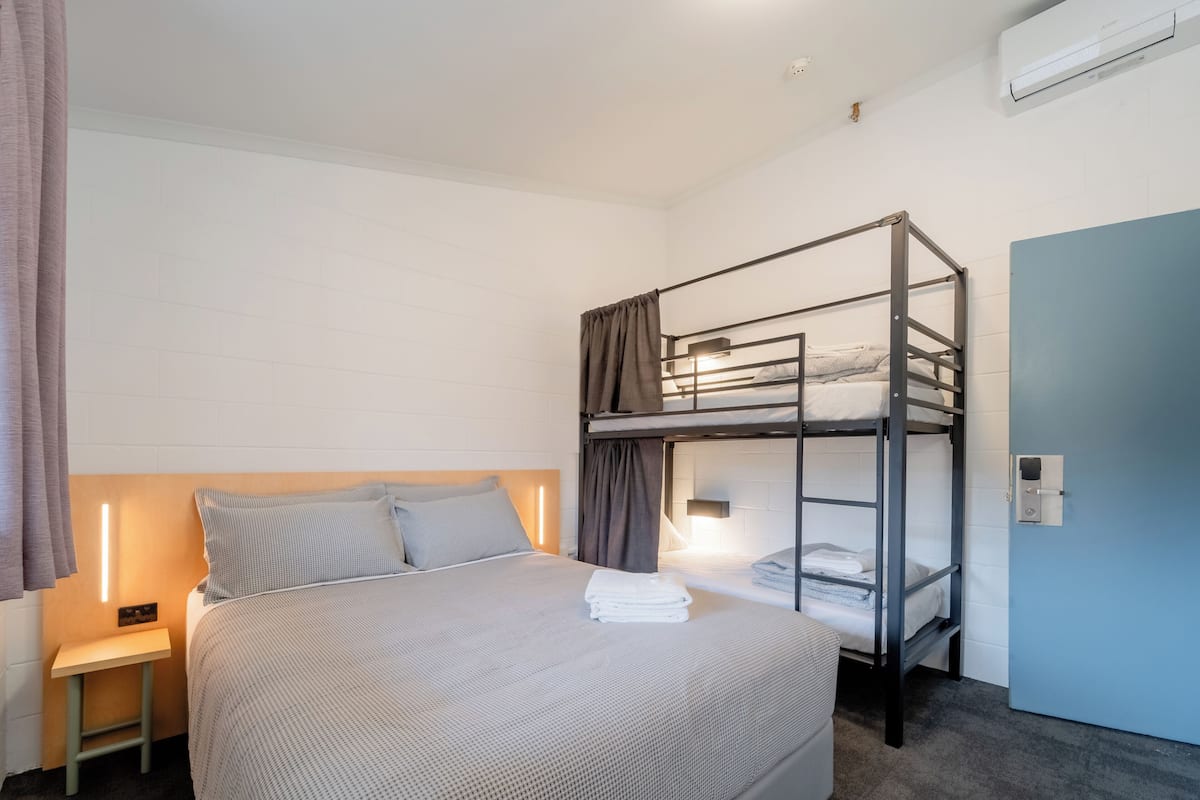 A bunk bed room with a single bed, a bedside table, and a door.