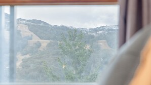 A view through a window with a wooden frame, a blurred landscape with trees and hills, and a glimpse of a building in the distance. - YHA Thredbo (Thredbo)