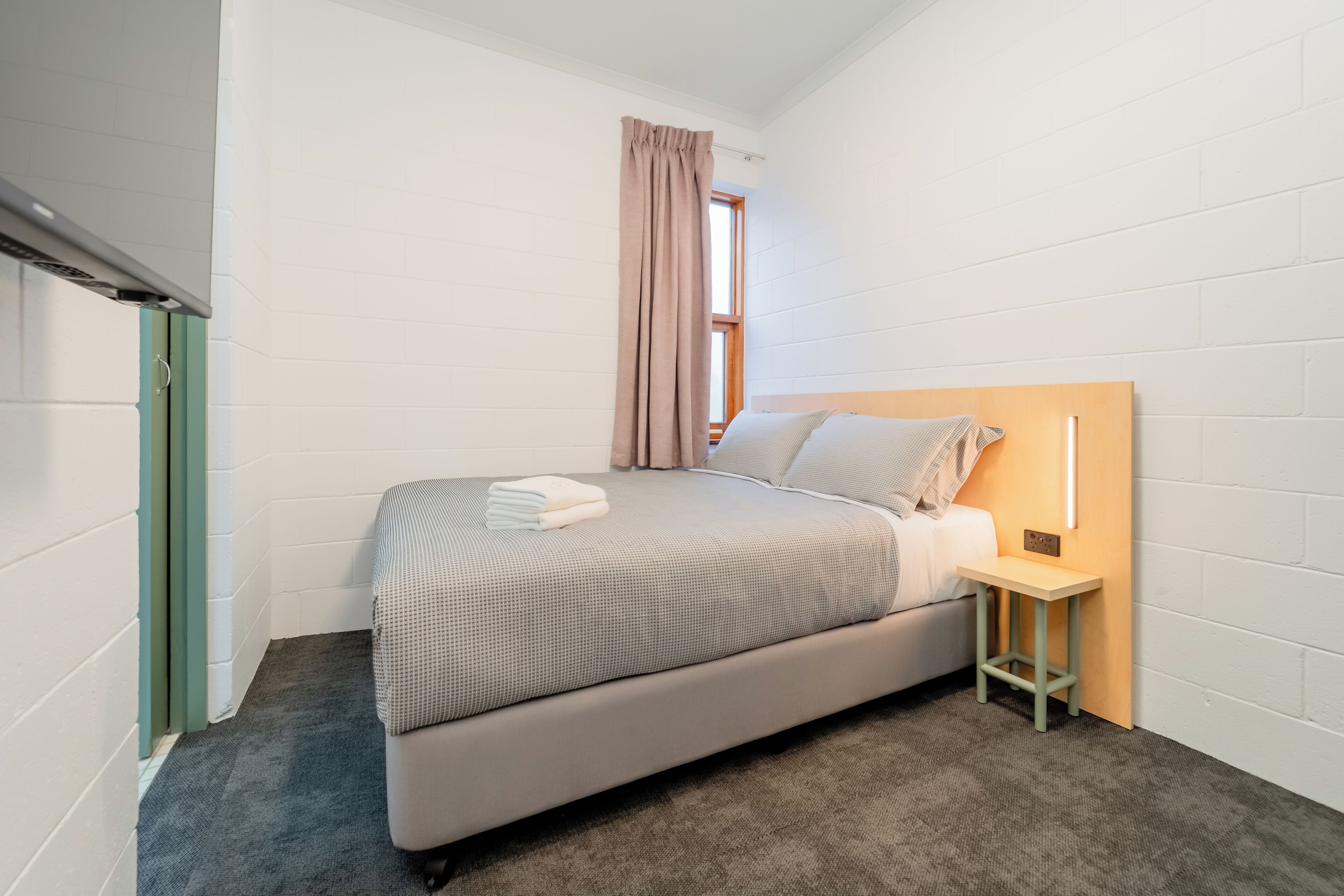 Une chambre à coucher comprenant un lit, une table de chevet, une fenêtre avec des rideaux et un luminaire fixé au mur.