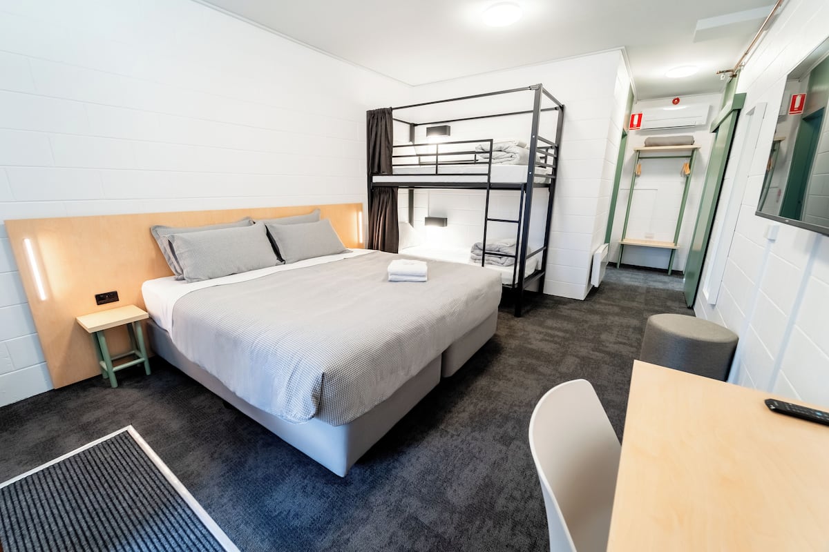 A bunk bed room with a desk and chair, a small stool, and a radiator.