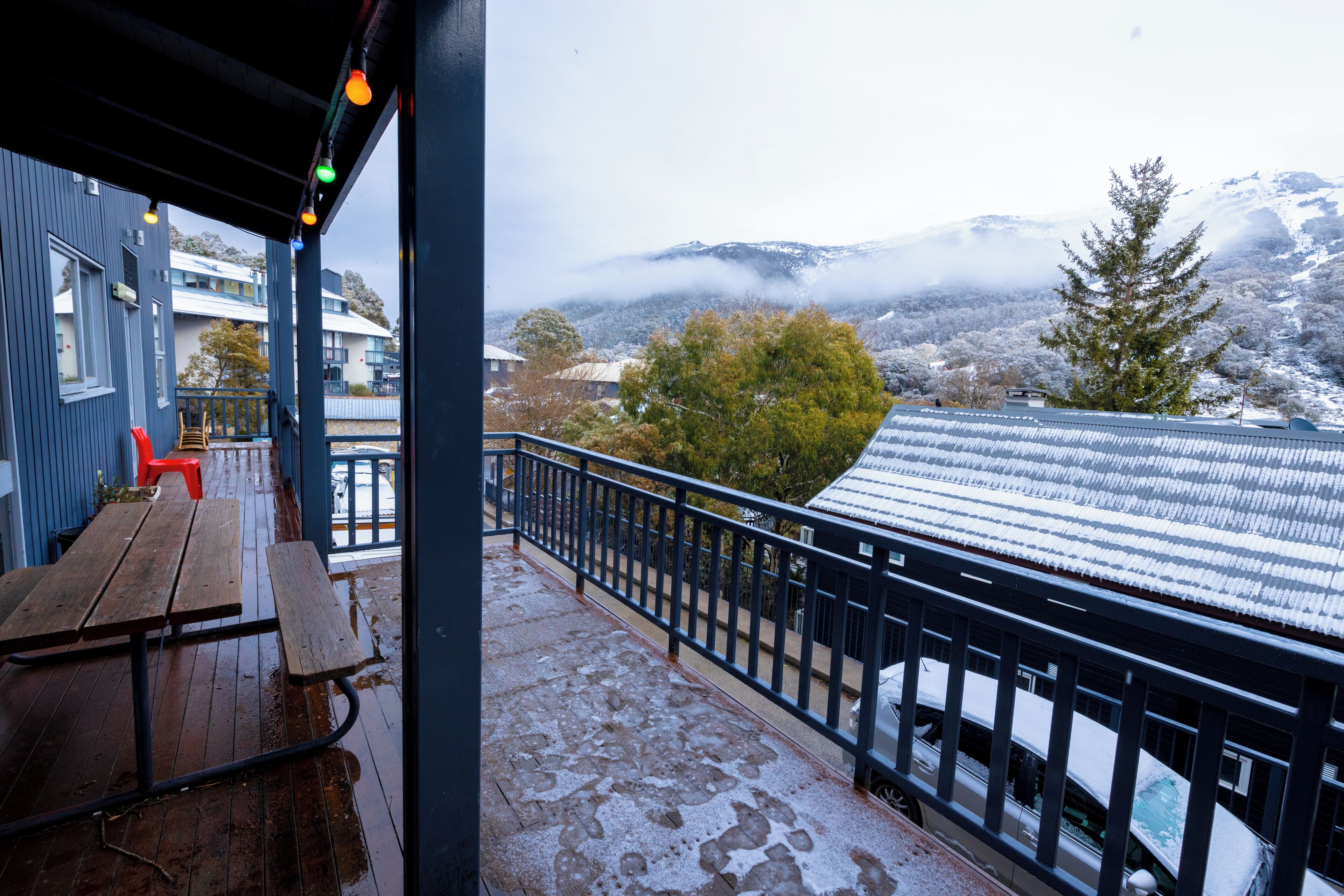A wooden deck with a metal railing, a red chair, and a view of snow-covered mountains and trees.