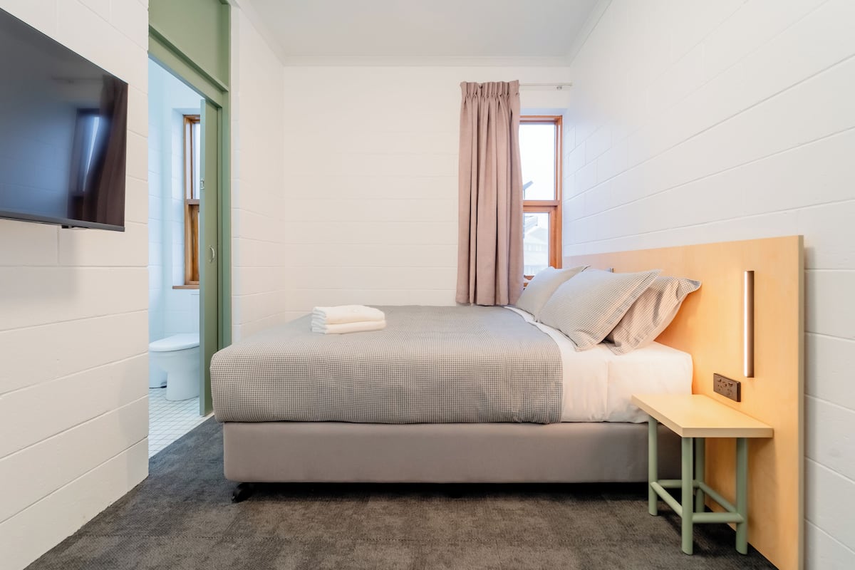 A modern bedroom with a bed, a bedside table, a TV mounted on the wall, and a window with curtains.
