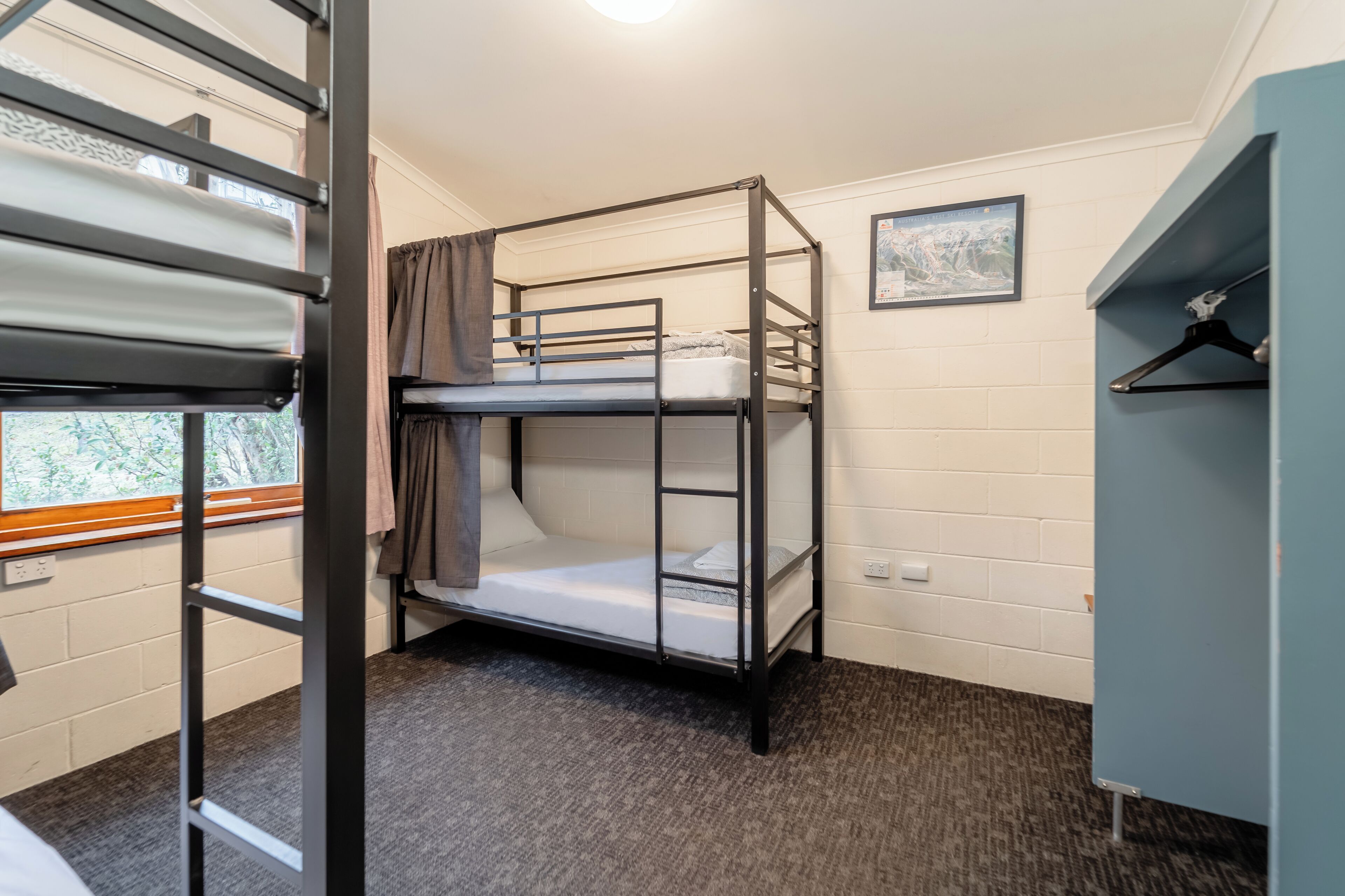 A bunk bed room with a window, a picture on the wall, and a wardrobe.