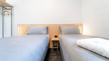 A twin room with two beds, a small table, and a hanging rack.
