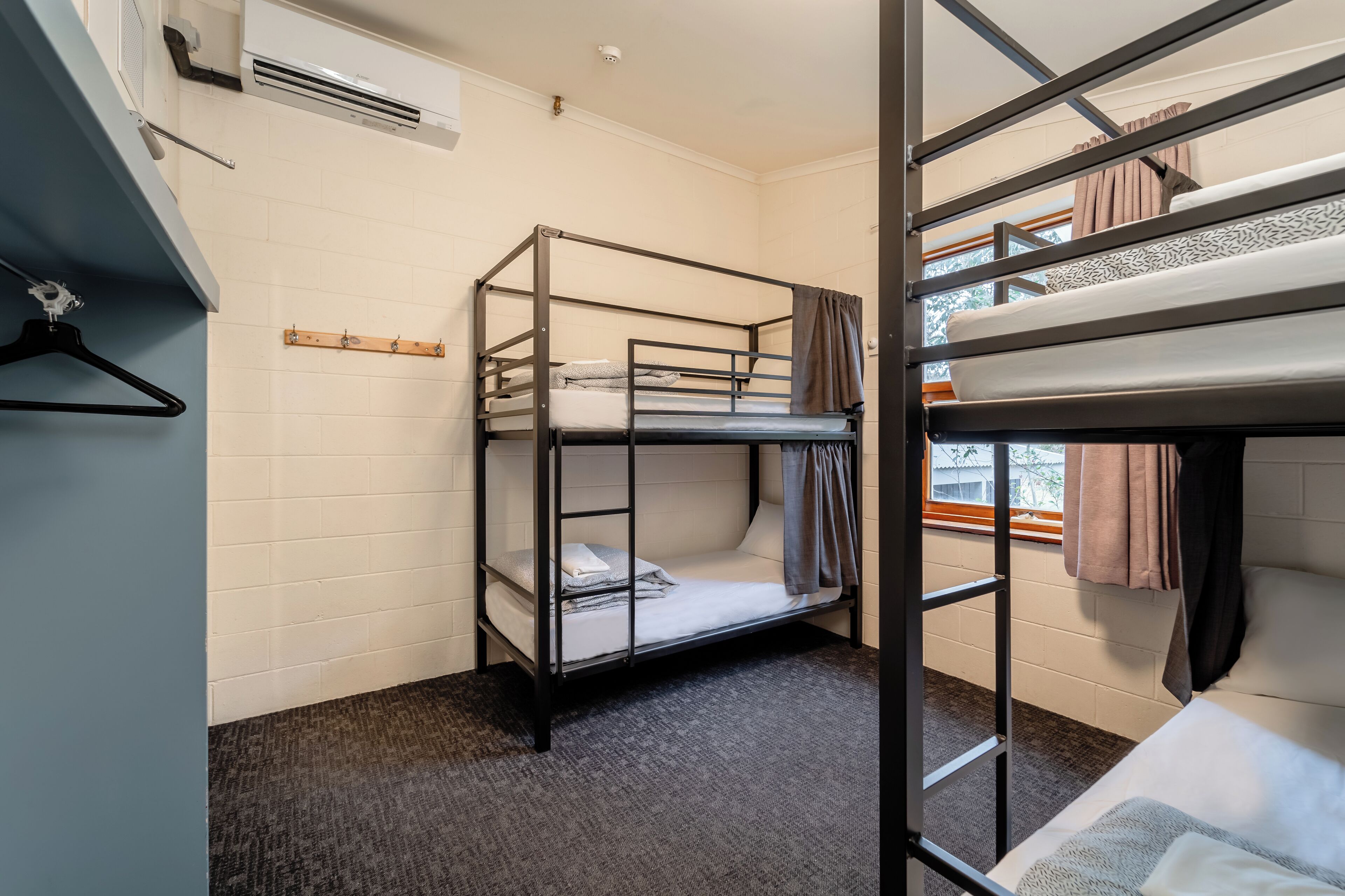 Habitación con literas, perchero, toallero y ventana con cortinas.