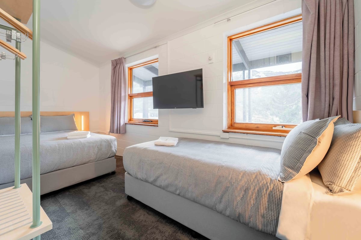 A hotel room with two beds, a flat-screen TV, large windows, and a view of the outdoors.
