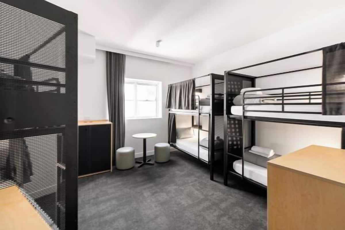A compact hotel room with bunk beds, a small round table, and a window with curtains.