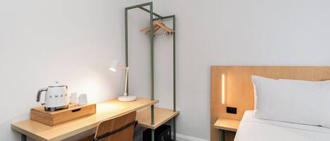 Une chambre d’hôtel avec un bureau en bois, une chaise, un lit avec une tête de lit en bois, un porte-manteau mural et une table de chevet avec une lampe.