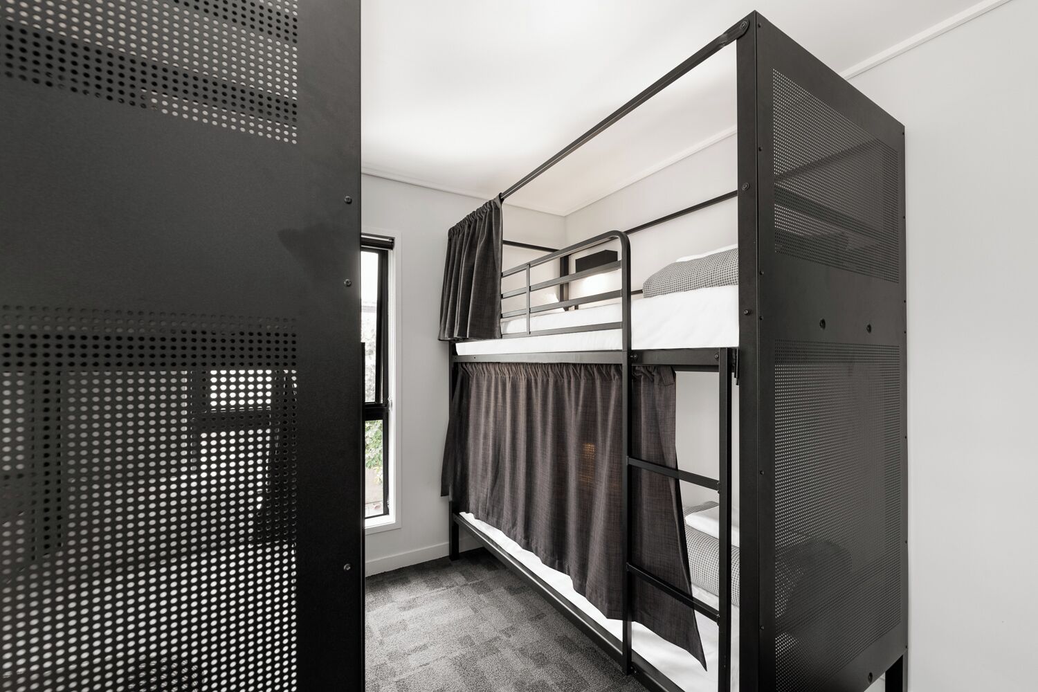 A bunk bed room with a metal frame, a window with curtains, and a door with a metal mesh.