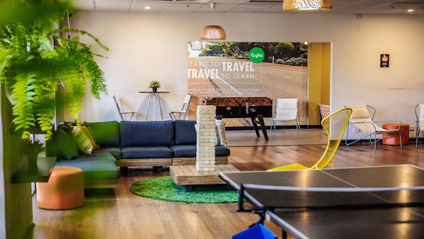 Un área de estar moderna con mesa de ping pong, asientos y un cartel grande que promociona viajes.