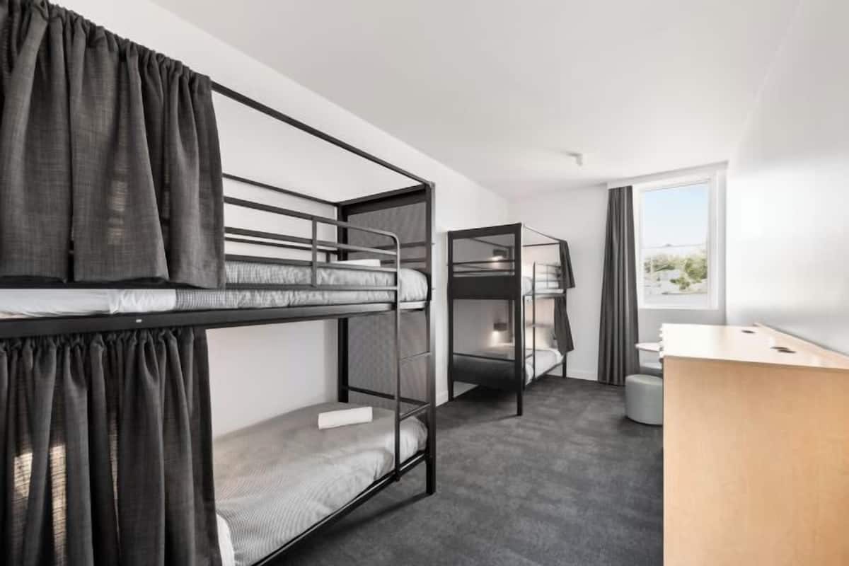 A modern hotel room with bunk beds, a desk, and a window with a view.