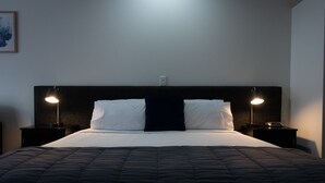 A neatly made bed with a dark quilt, two white pillows, and two bedside lamps on either side. - Cambridge Mews (Cambridge)