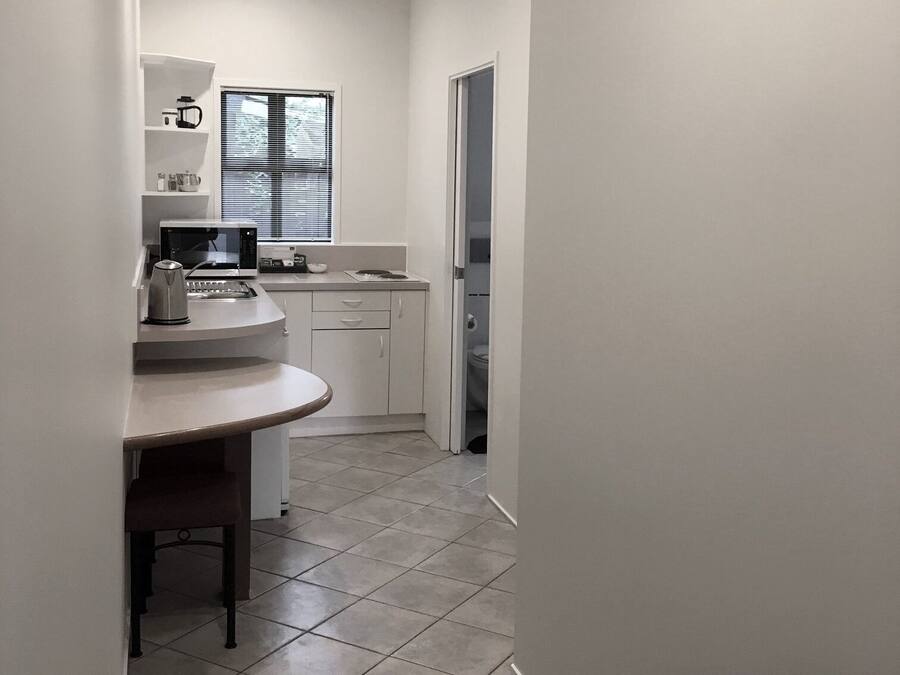 A compact kitchen with a countertop, a kettle, and a window with blinds.