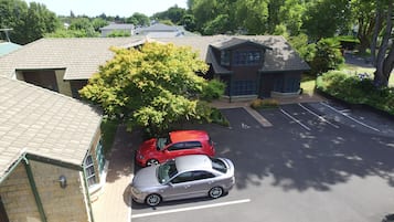 Een parkeerplaats met twee auto's, een gebouw met een bakstenen gevel en een boom op de voorgrond.