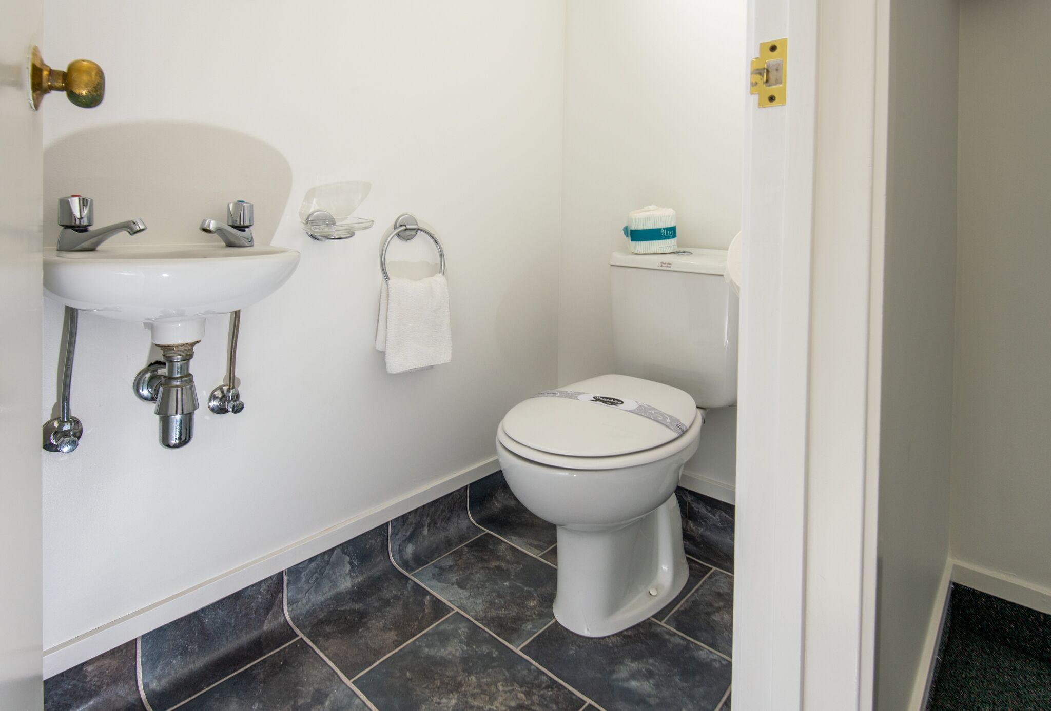 A bathroom with a white sink, chrome faucets, a white toilet, and dark tiled flooring.