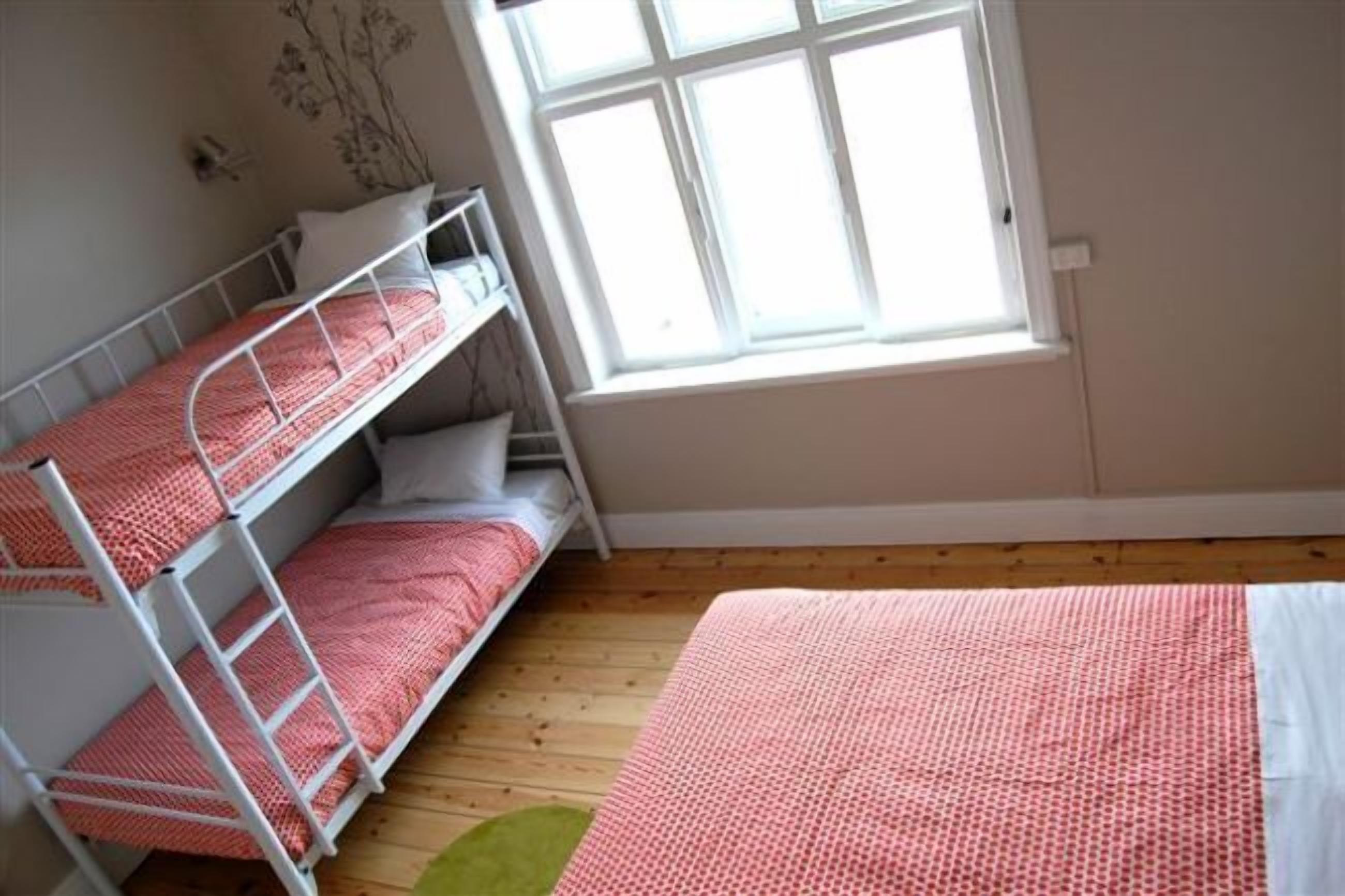 Quarto com beliches, janela e piso de madeira.