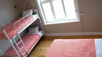 Quarto com beliches, janela e piso de madeira.