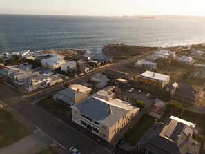 An aerial view of a coastal residential area with houses, a road, and a cliff overlooking the sea. - YHA Port Elliot (Port Elliot)
