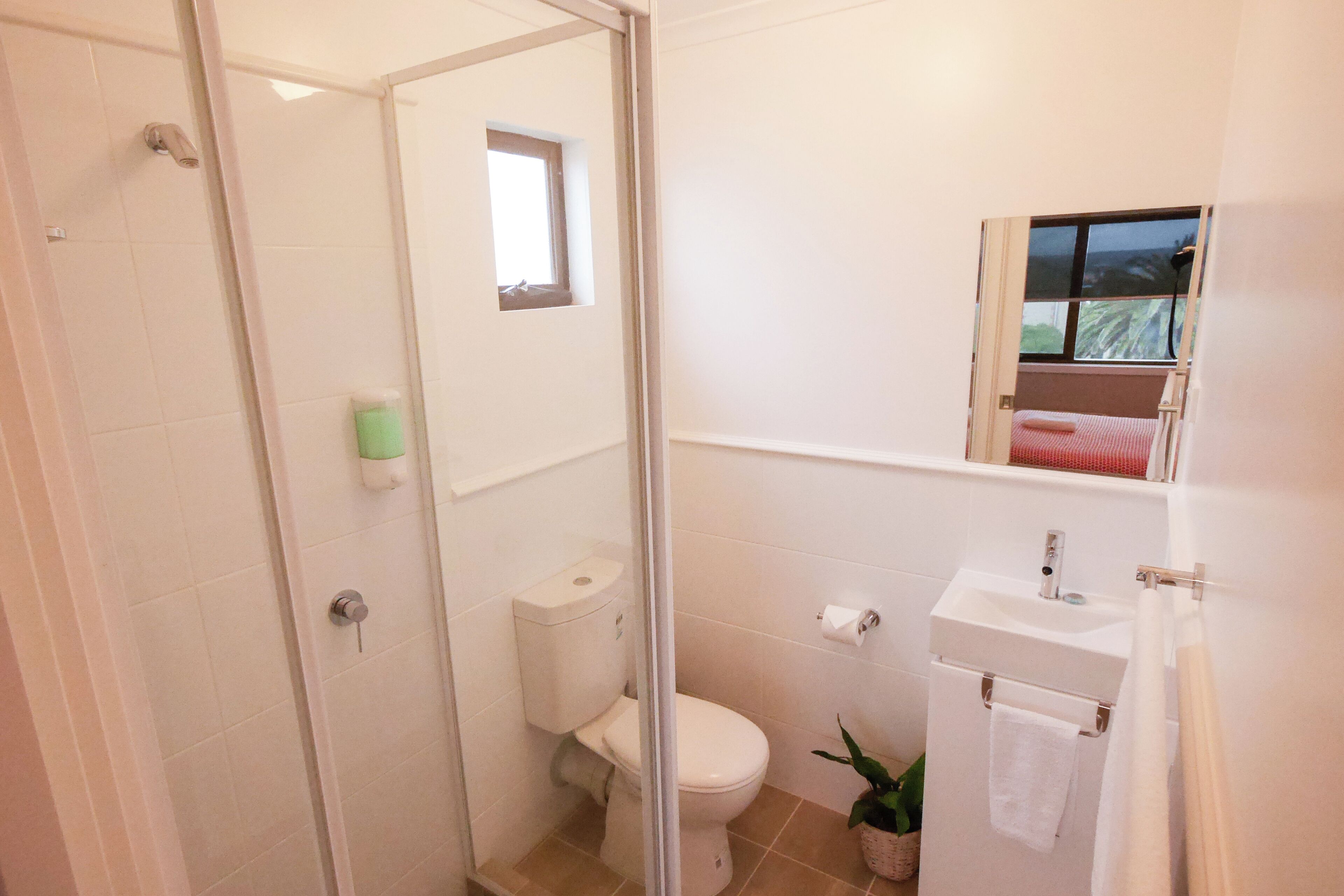A bathroom with a glass-enclosed shower, a toilet, a sink, and a small window.