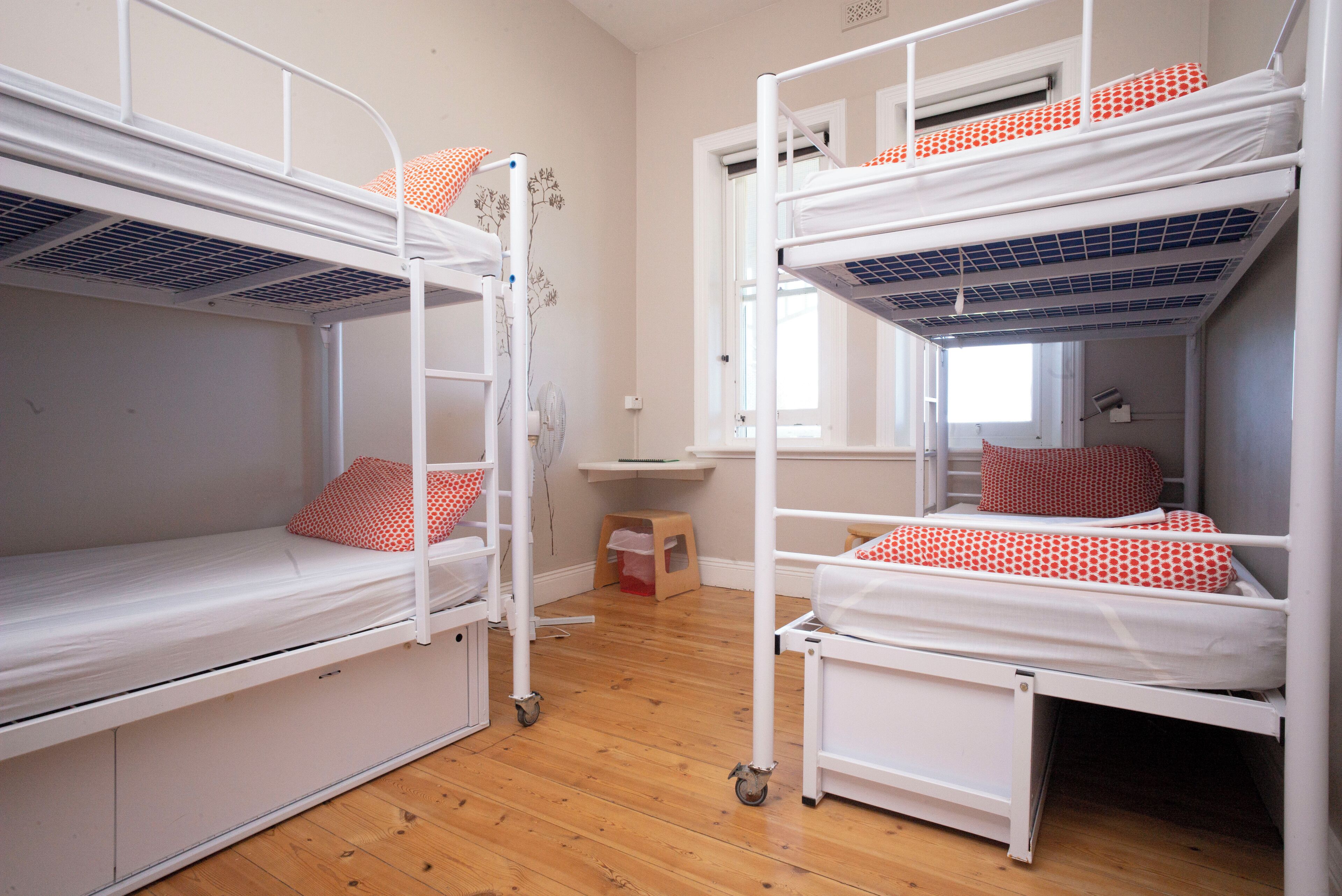 Una habitación con dos literas, suelo de madera, una mesita y una ventana.