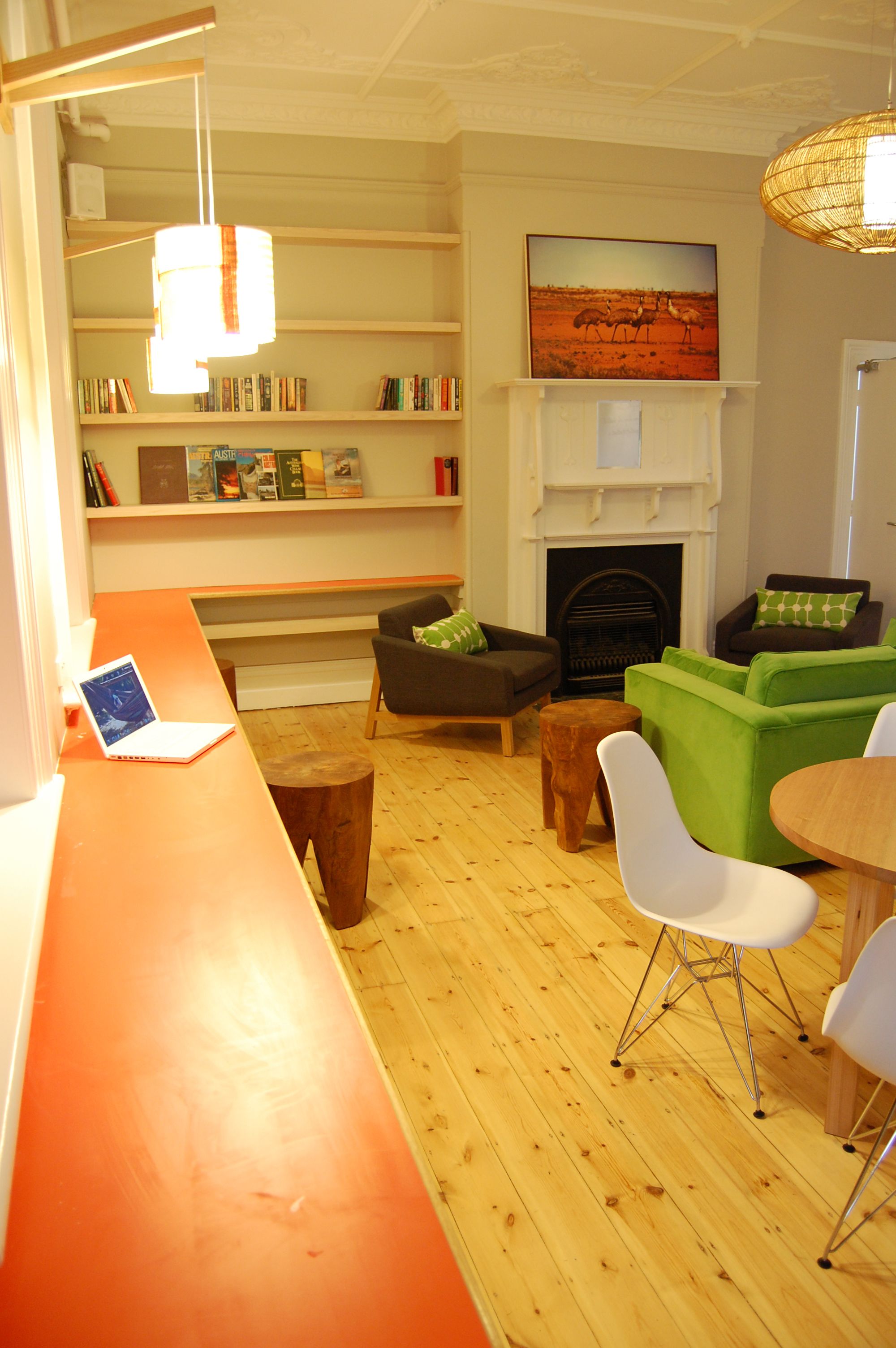 A modern living room with a wooden floor, a fireplace, a bookshelf, and a laptop on a table.