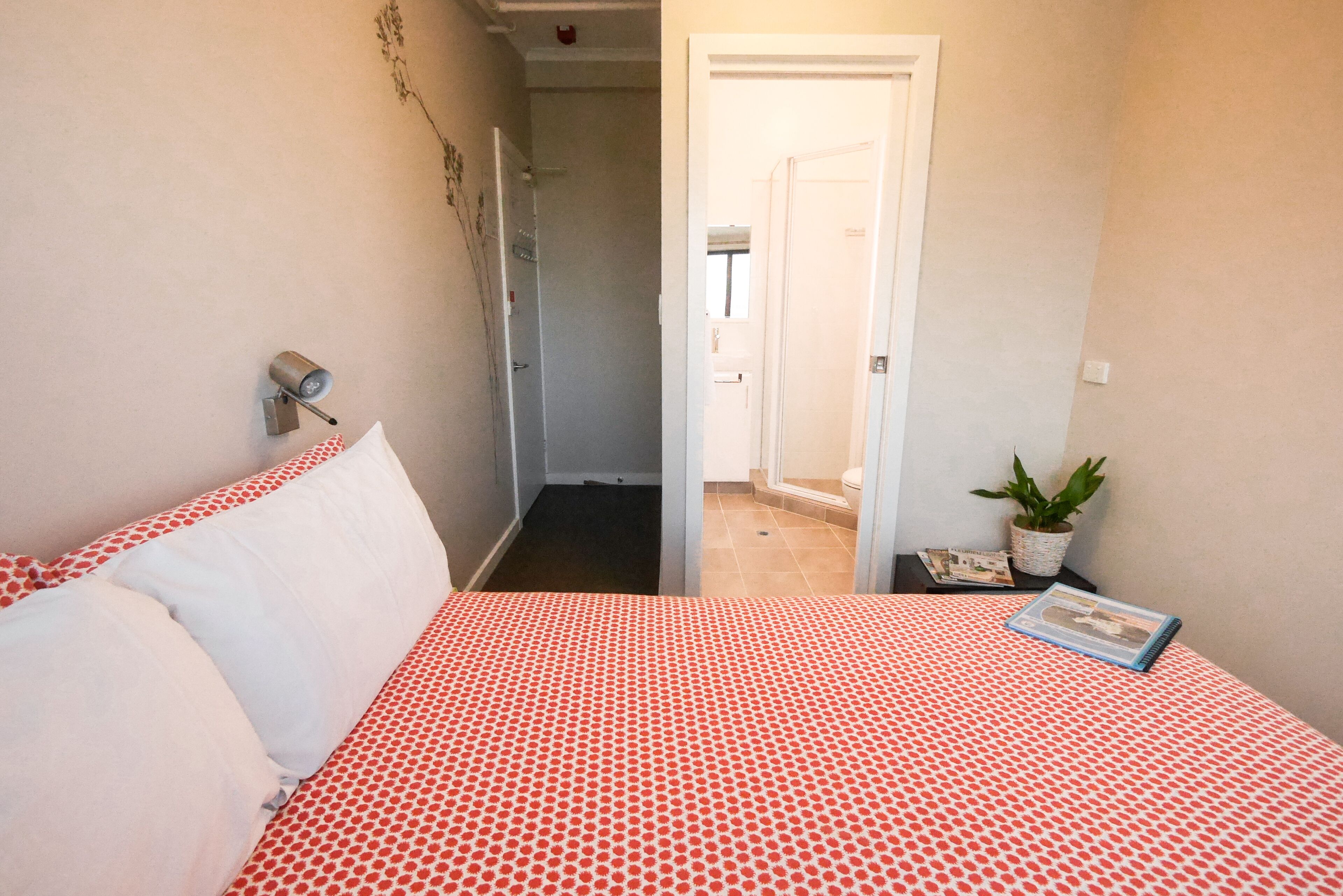 A bedroom with a bed, a nightstand, a wall-mounted lamp, and a door leading to a bathroom.