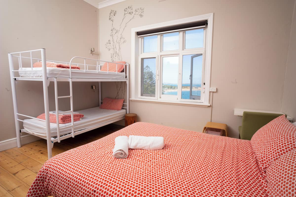 A bunk bed with a red and white polka dot bedspread, a window with a view of the sea, and a small wooden stool.