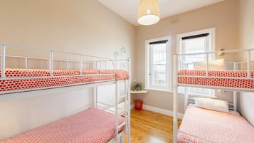 Una habitación con literas, una ventana, una planta y una lámpara colgante.