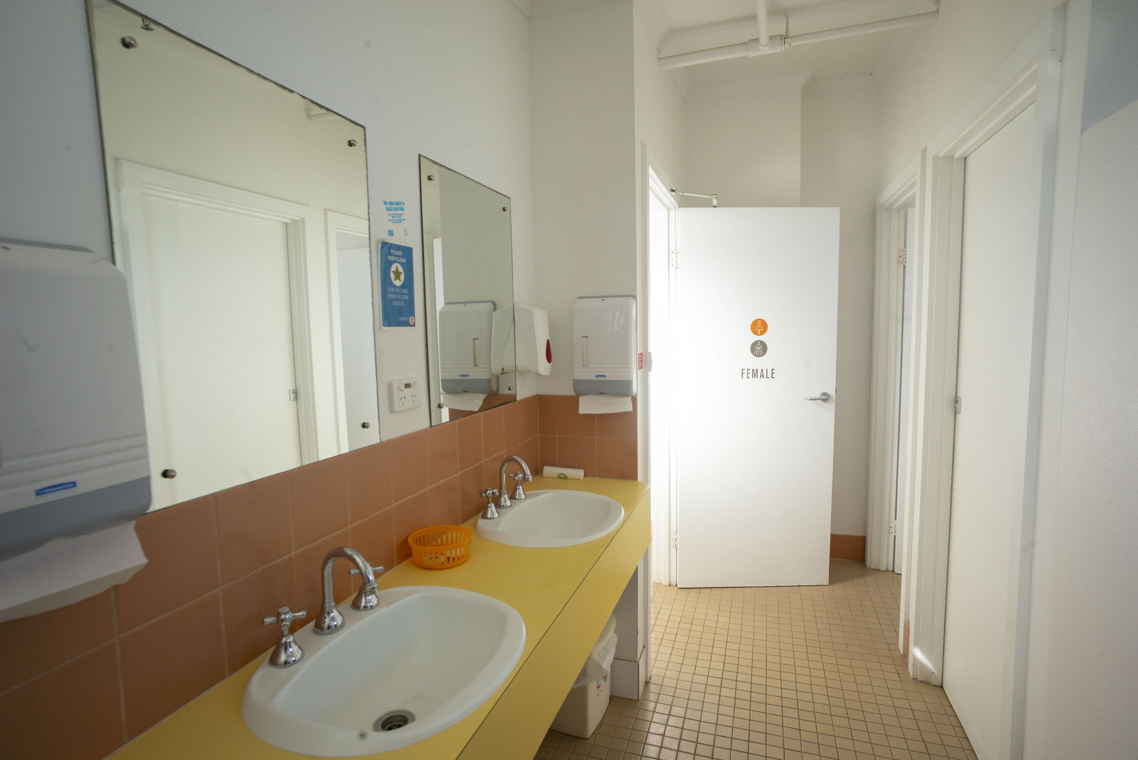 Un baño con dos lavamanos, un espejo y una puerta que indica 'FEMALE'.