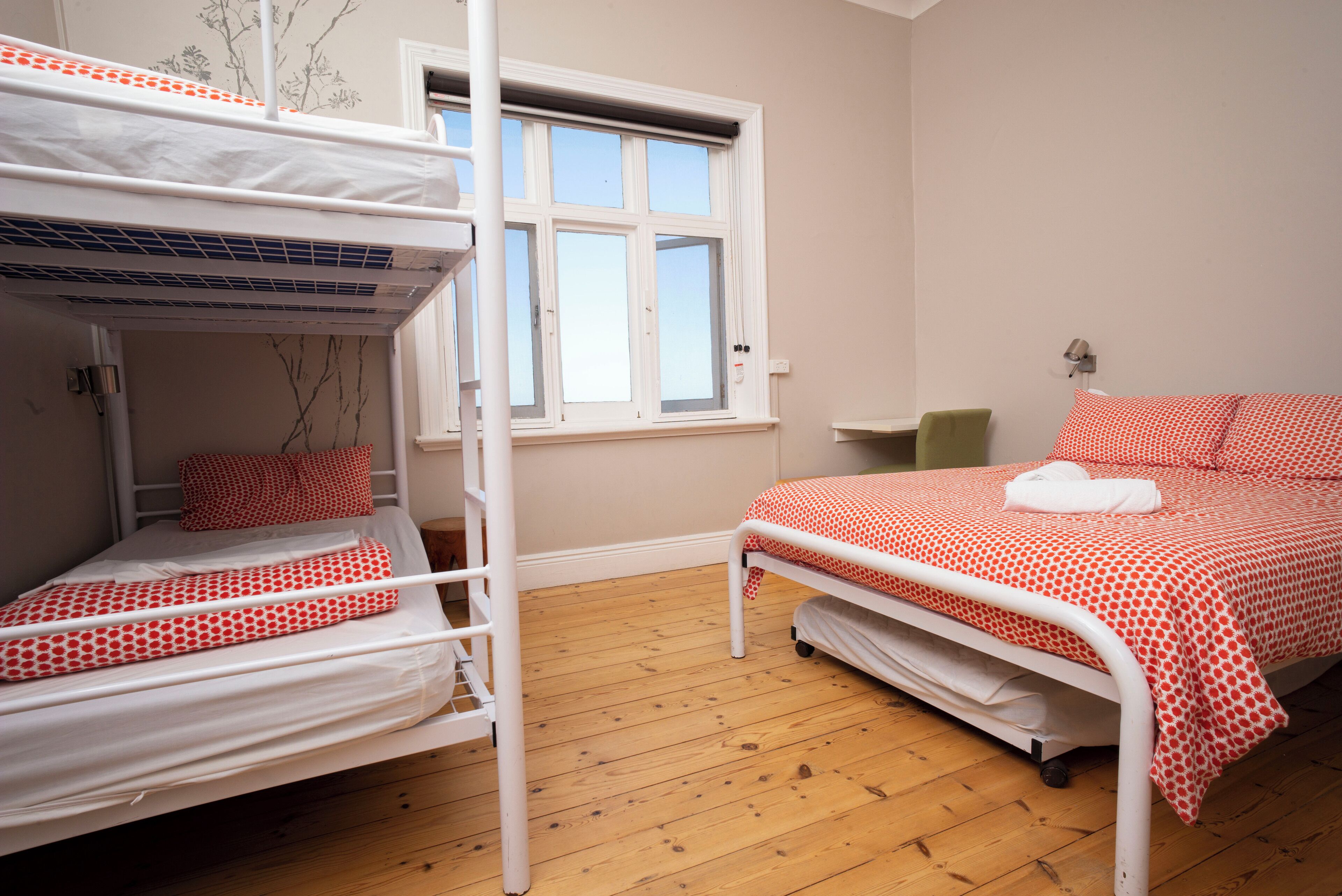Una habitación con literas, una ventana, una mesita de noche y una cama con colcha roja de lunares.